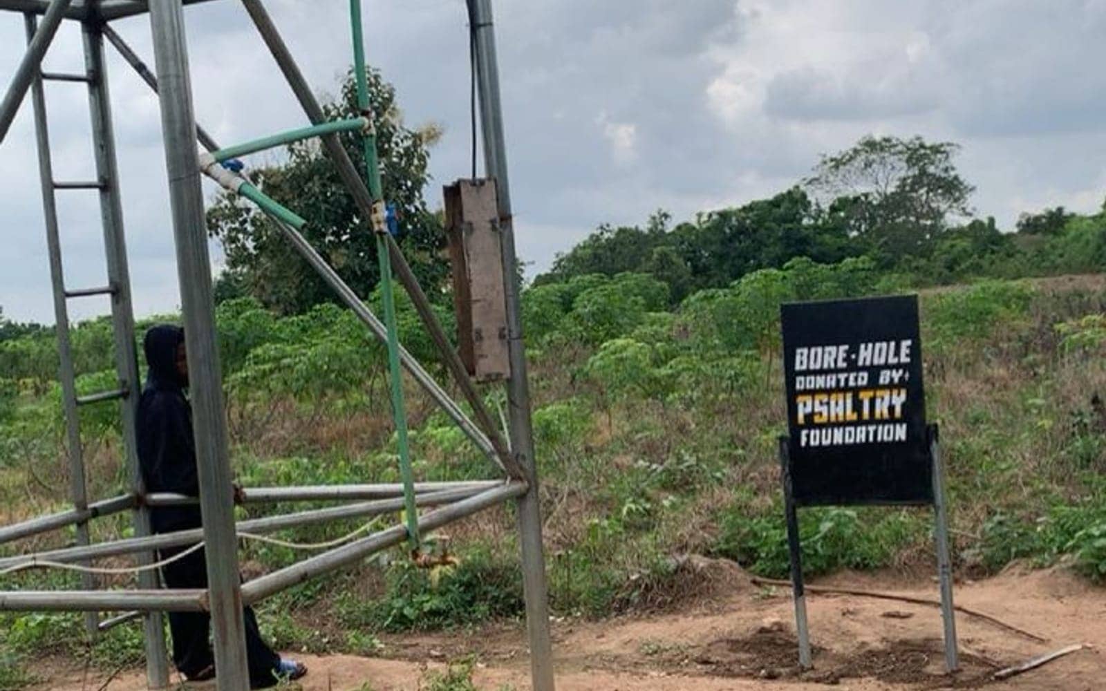 A borehole and overhead tank installed by Psaltry Foundation, with a “Borehole donated by Psaltry Foundation” sign, in a farming community